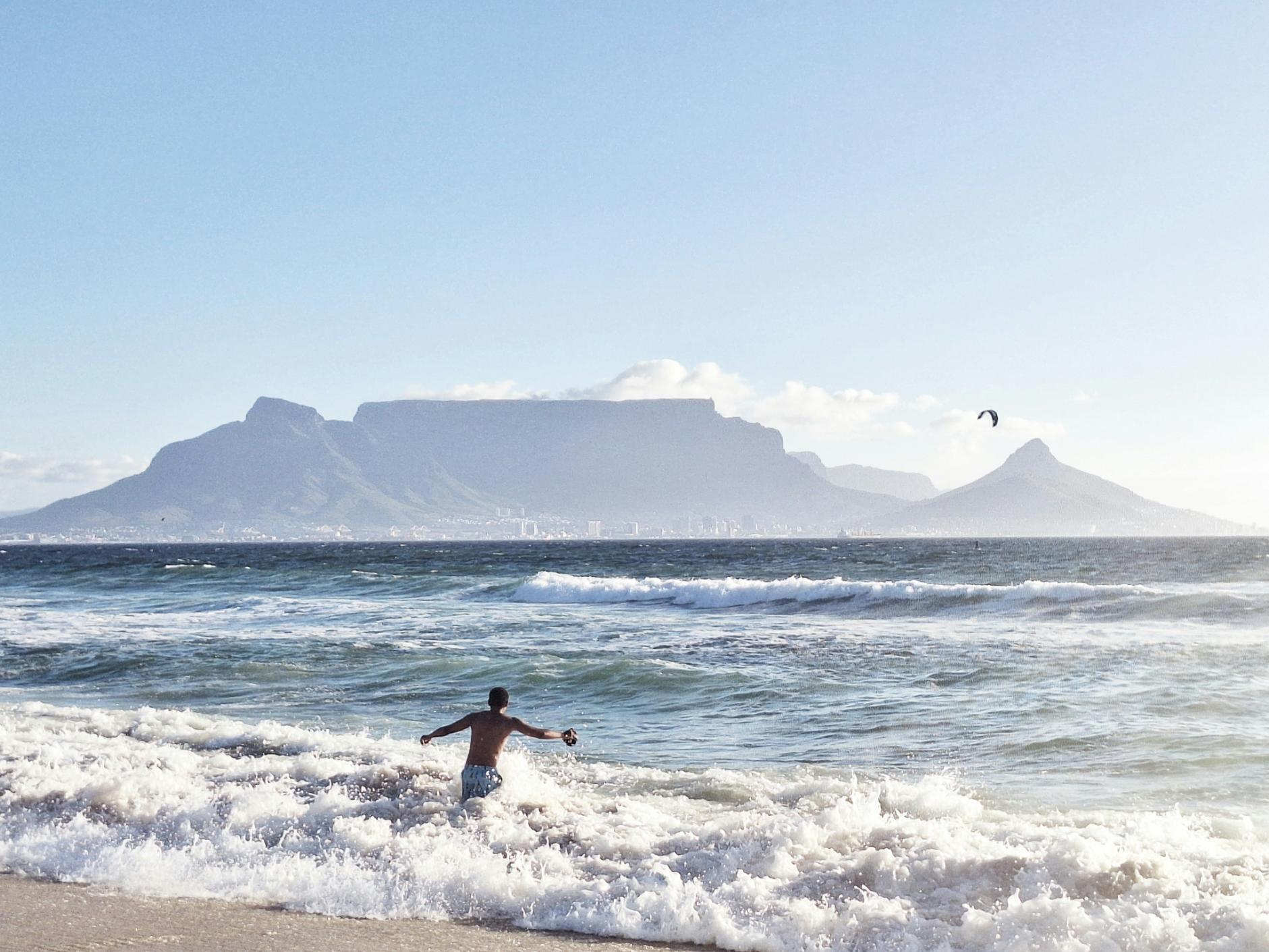 Person jumping into the waves at Bloubergstrand Beach