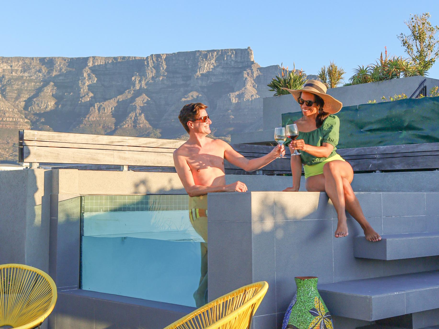 A man and a woman poolside toasting, with Table Mountain in the background.