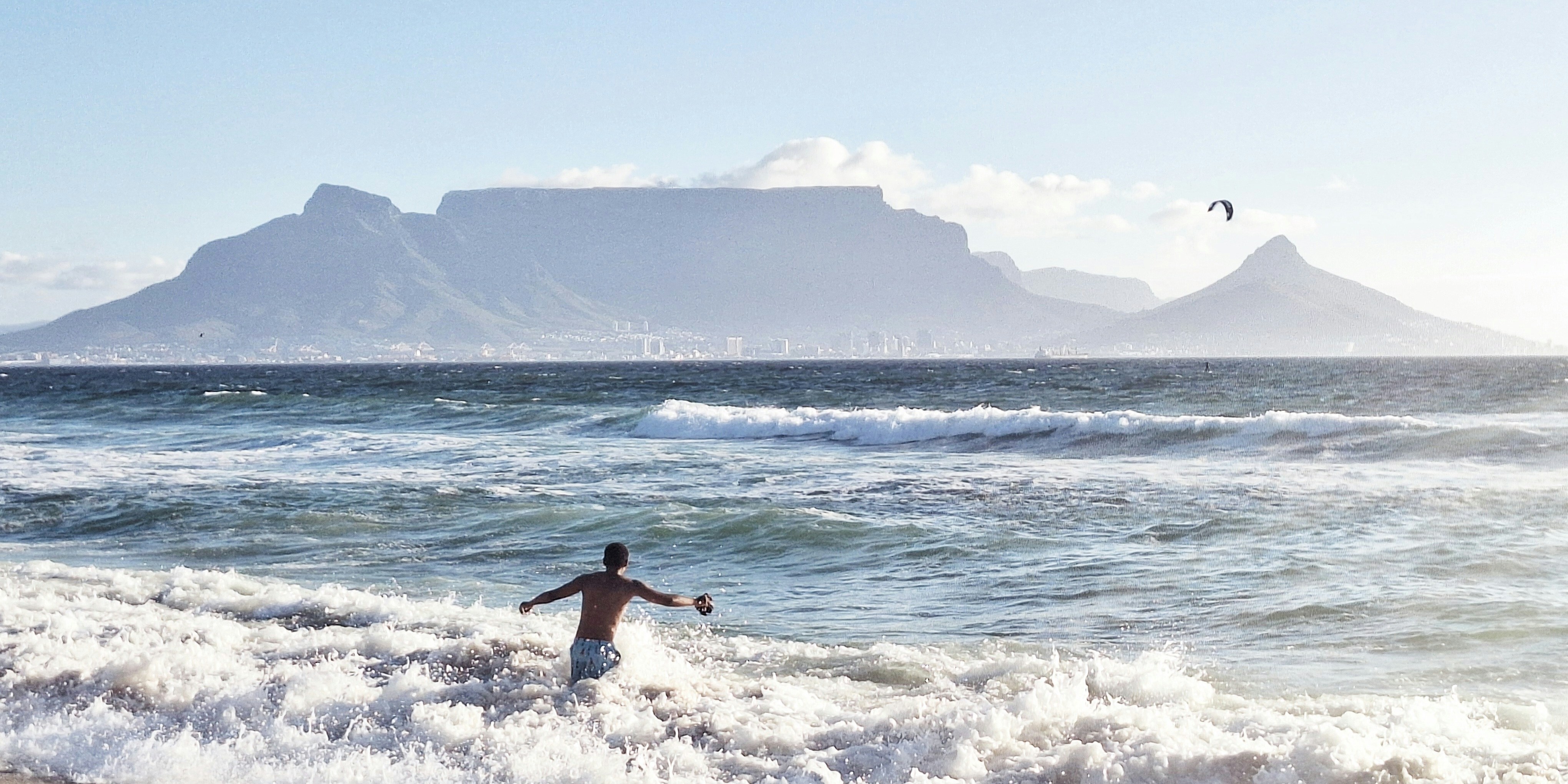Boy jumping into waves at Blouberg Beach, with Table Mountain in the background